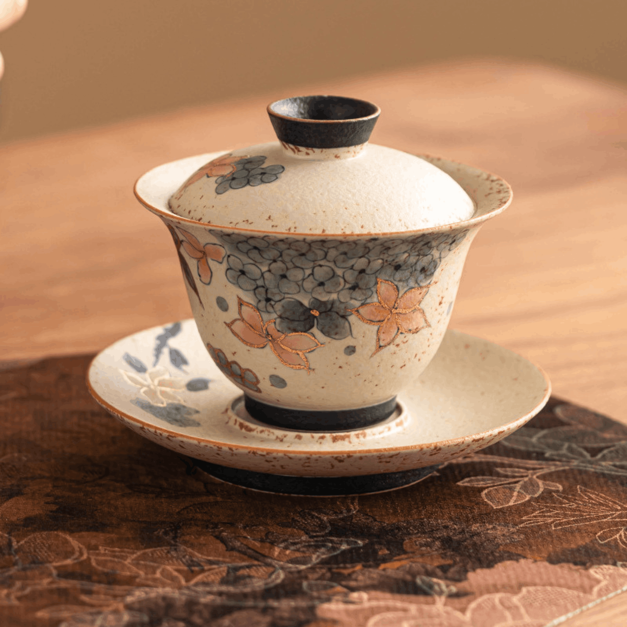 Decorative ceramic gaiwan with floral patterns on a textured surface