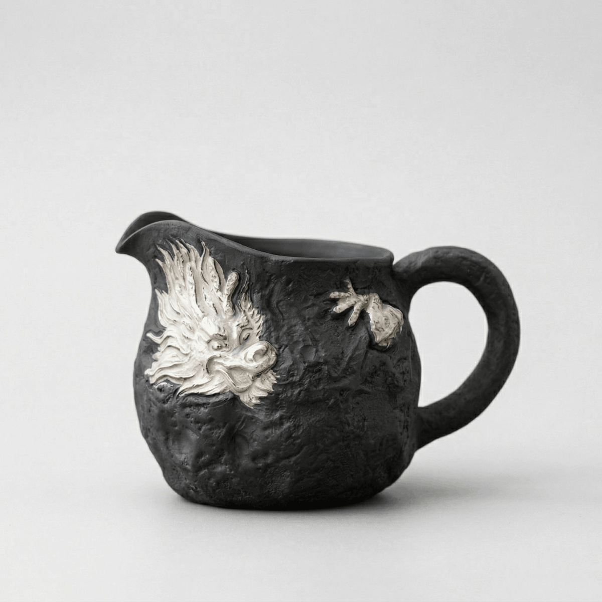 Black ceramic pitcher with silver dragon design on a white background