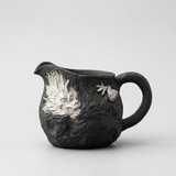 Black ceramic pitcher with silver dragon design on a white background