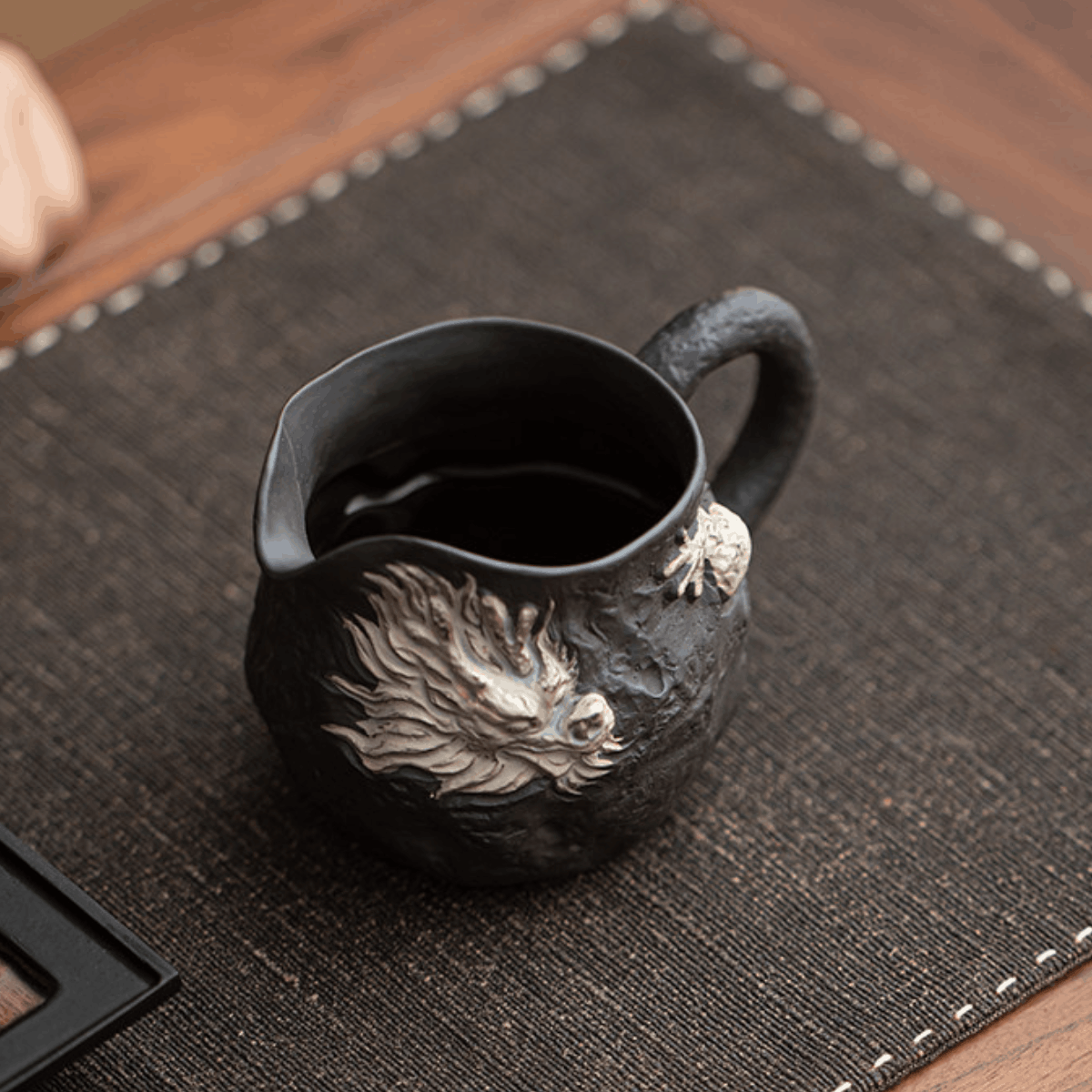 Black ceramic mug with dragon design on a dark textured mat