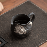 Black ceramic mug with dragon design on a dark textured mat