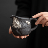 Person holding a black ceramic pitcher with dragon design against a dark background