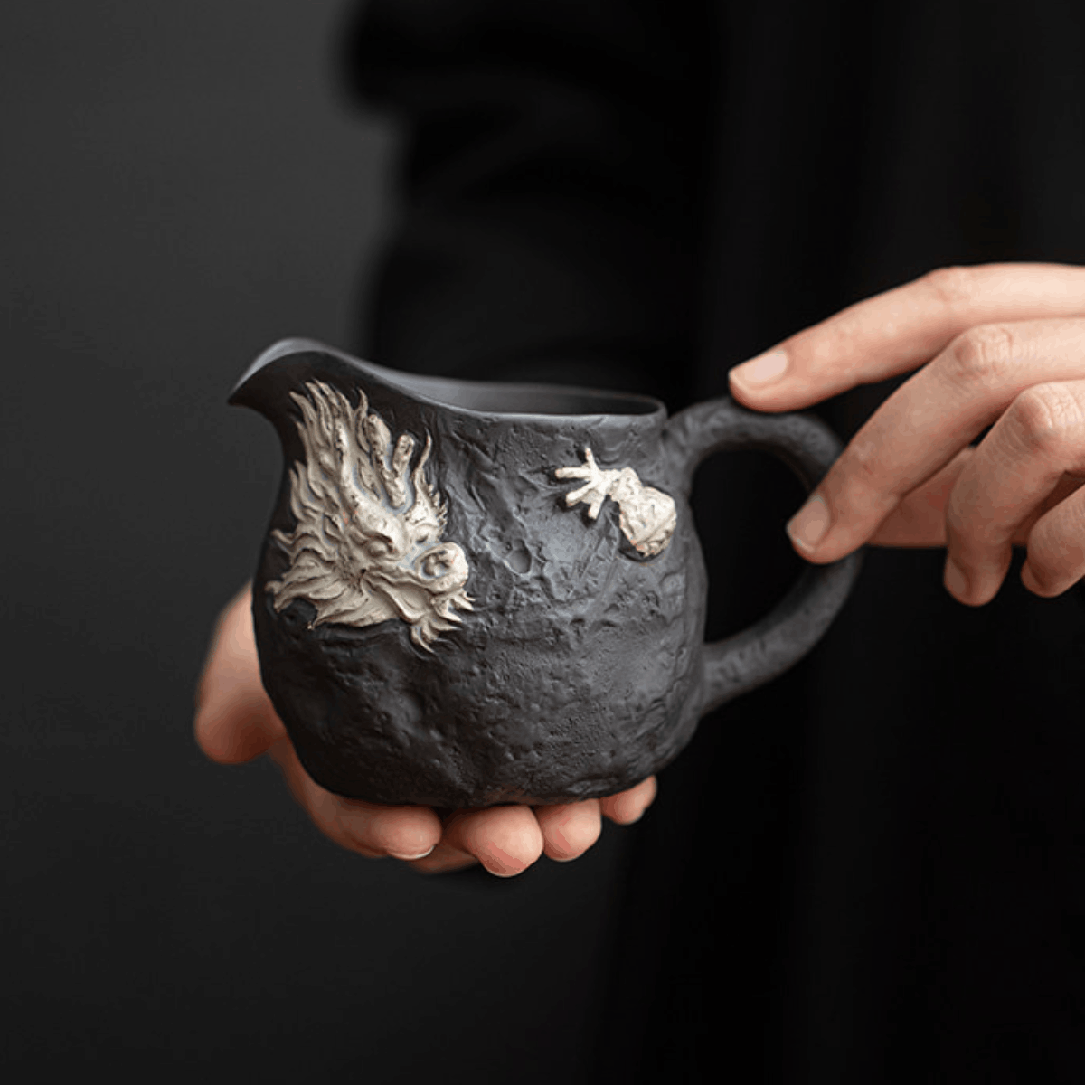 Person holding a black ceramic pitcher with dragon design against a dark background